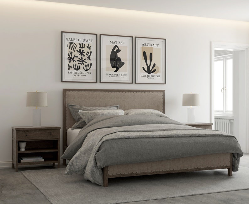 May include: A gray upholstered bed with a headboard featuring a tufted design and nailhead trim. The bed is made up with gray bedding and two white pillows. Three framed art prints hang above the headboard, featuring abstract designs and the text "Galerie d'Art", "Matisse", and "Abstract".