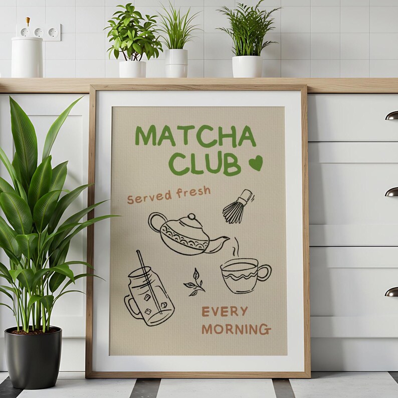 Pu&ograve; includere: Una stampa incorniciata con le parole "Matcha Club" in verde, insieme a illustrazioni di una teiera, una frusta e una tazza. Sono inclusi anche i testi "Served fresh" e "Every morning". La stampa ha uno sfondo beige e una cornice in legno.