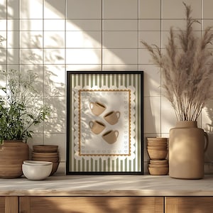 May include: A framed print featuring four beige coffee cups on a white background with a scalloped border of hearts. The print has a green and white striped background. The print is displayed on a wooden surface.
