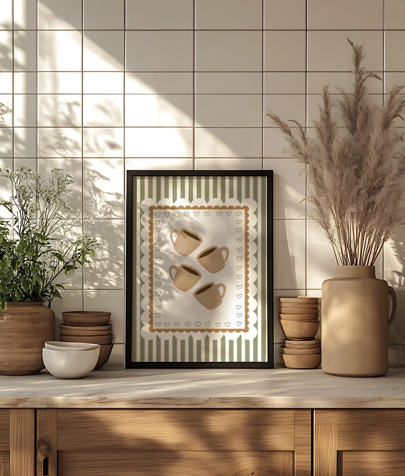 May include: A framed print featuring four beige coffee cups on a white background with a scalloped border of hearts. The print has a green and white striped background. The print is displayed on a wooden surface.