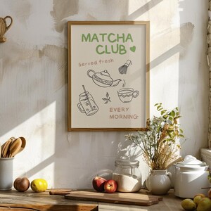 Pu&ograve; includere: Una stampa incorniciata con il testo "Matcha Club" e illustrazioni di articoli relativi al matcha. La stampa presenta una teiera, una frusta, una tazza e una bevanda in un bicchiere. Sono incluse anche le parole "Servito fresco" e "Ogni mattina".