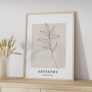 K&ouml;nnte beinhalten: Ein gerahmter Druck mit einer minimalistischen Linienzeichnung eines Zweigs mit Bl&auml;ttern auf beigefarbenem Hintergrund. Der Text "ARTISTRY simplicit&eacute;" ist unter der Zeichnung gedruckt.