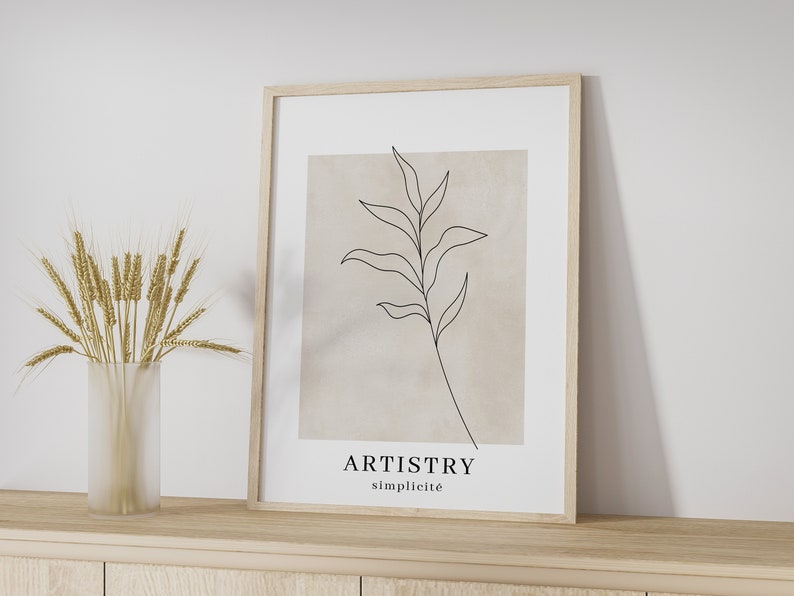 K&ouml;nnte beinhalten: Ein gerahmter Druck mit einer minimalistischen Linienzeichnung eines Zweigs mit Bl&auml;ttern auf beigefarbenem Hintergrund. Der Text "ARTISTRY simplicit&eacute;" ist unter der Zeichnung gedruckt.