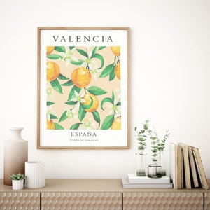 Op de afbeelding: Een ingelijst afdruk met een aquarel-illustratie van sinaasappelbloesems en sinaasappelen. De afdruk bevat de tekst "Valencia, Espa&ntilde;a, Tierra de Naranjas" in zwart.
