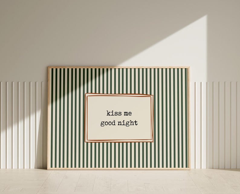 Puede incluir: Arte de pared enmarcado con un fondo a rayas verdes y blancas. La obra de arte presenta una secci&oacute;n rectangular de color crema con las palabras "kiss me good night" en negro, en una fuente de estilo m&aacute;quina de escribir. El marco es de color madera clara.