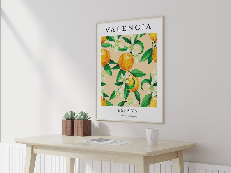 Op de afbeelding: Een ingelijste poster met een aquarel-illustratie van sinaasappelbloesems en sinaasappelen. De poster heeft de tekst "Valencia, Espa&ntilde;a, Tierra de Naranjas" erop gedrukt.