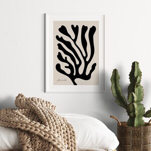 May include: A black and white abstract print of a stylized coral branch on a beige background. The print is framed in a white frame.