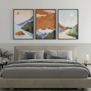 Pode incluir: Tr&ecirc;s impress&otilde;es emolduradas de paisagens abstratas com montanhas, &aacute;gua e c&eacute;u em estilo aquarela em tons de azul, verde, laranja e marrom. As impress&otilde;es est&atilde;o penduradas acima de uma cama estofada cinza com roupa de cama branca.