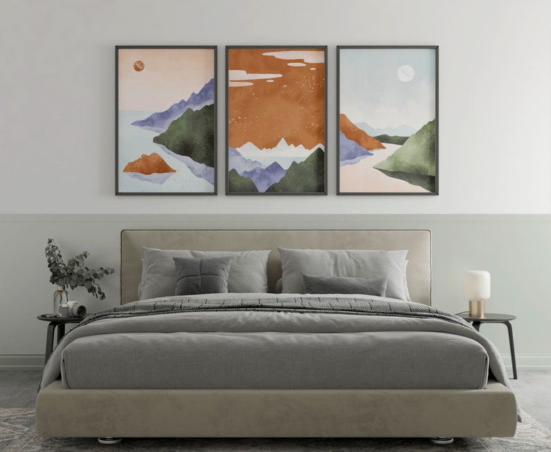 Pode incluir: Tr&ecirc;s impress&otilde;es emolduradas de paisagens abstratas com montanhas, &aacute;gua e c&eacute;u em estilo aquarela em tons de azul, verde, laranja e marrom. As impress&otilde;es est&atilde;o penduradas acima de uma cama estofada cinza com roupa de cama branca.