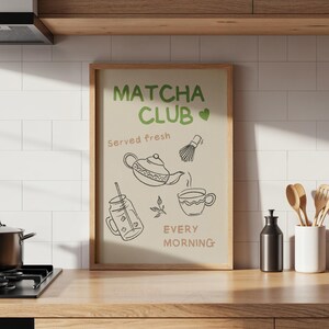 Pu&ograve; includere: Una stampa incorniciata con le parole "Matcha Club" in verde e "Served fresh" e "Every morning" in marrone chiaro. La stampa presenta disegni a tratto di oggetti legati al matcha, tra cui una teiera, una frusta e una tazza.
