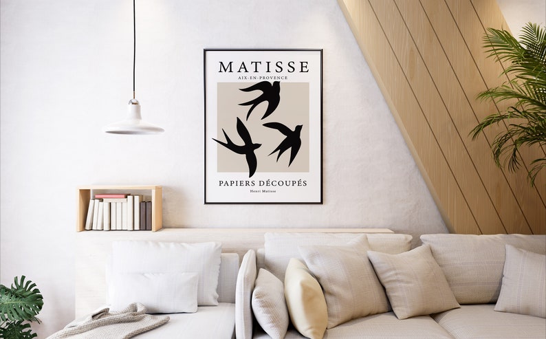 May include: A framed art print featuring a minimalist design with three black bird silhouettes against a beige background. The print includes the text "MATISSE AIX-EN-PROVENCE PAPIERS D&Eacute;COUP&Eacute;S" in black font. The artwork is displayed in a modern living room setting.