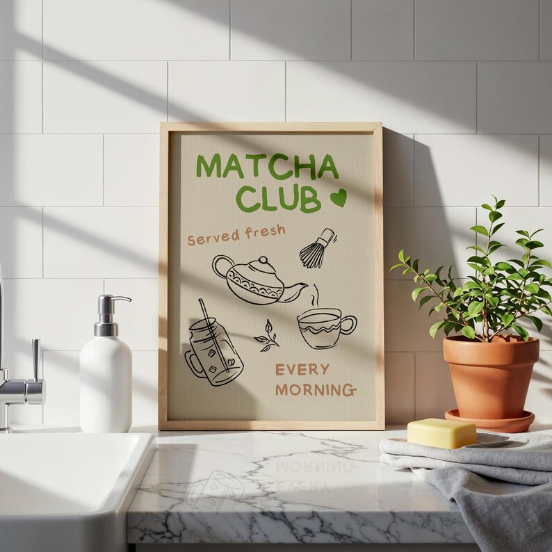 Pu&ograve; includere: Una stampa incorniciata con le parole "Matcha Club" in verde, insieme a illustrazioni di strumenti per la preparazione del t&egrave; matcha. &Egrave; incluso anche il testo "Servito fresco" e "Ogni mattina". La stampa &egrave; esposta su una superficie piastrellata bianca.