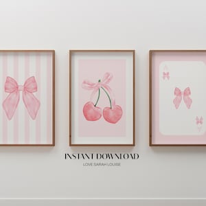 Puede incluir: Tres impresiones de arte de pared imprimibles en rosa y blanco con un lazo rosa, un lazo rosa con cerezas y un lazo rosa con un as de picas de carta de juego. Las impresiones están en marcos marrones.