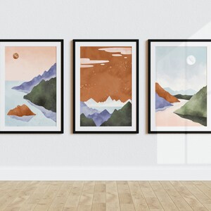 Pode incluir: Tr&ecirc;s pinturas em aquarela emolduradas que retratam paisagens abstratas com montanhas, &aacute;gua e um c&eacute;u com uma lua ou sol. As pinturas est&atilde;o em molduras pretas e est&atilde;o penduradas em uma parede branca.