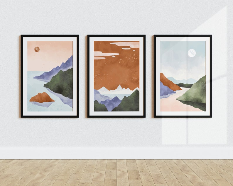 Pode incluir: Tr&ecirc;s pinturas em aquarela emolduradas que retratam paisagens abstratas com montanhas, &aacute;gua e um c&eacute;u com uma lua ou sol. As pinturas est&atilde;o em molduras pretas e est&atilde;o penduradas em uma parede branca.