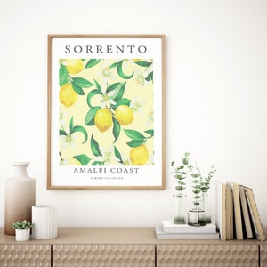 May include: A framed print with a yellow background and a pattern of green leaves, white flowers, and yellow lemons. The text "SORRENTO AMALFI COAST ALBERO DI LIMONE" is printed on the print.