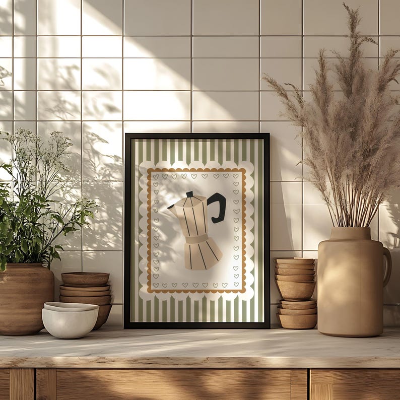 Peut inclure: Une affiche encadr&eacute;e repr&eacute;sentant une cafeti&egrave;re beige et noire. L'illustration est plac&eacute;e sur un fond &agrave; rayures vertes et blanches, avec une bordure festonn&eacute;e et des c&oelig;urs. L'affiche est expos&eacute;e sur une surface en bois, avec d'autres &eacute;l&eacute;ments d&eacute;coratifs.