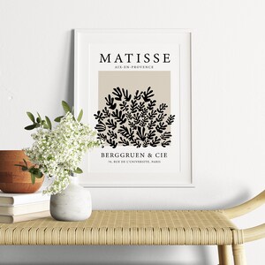 May include: A black and white art print featuring a stylized image of leaves in a beige background. The print has the text "MATISSE" at the top, "AIX-EN-PROVENCE" below it, and "BERGGRUEN & CIE" and "79, RUE DE L'UNIVERSITE, PARIS" at the bottom.