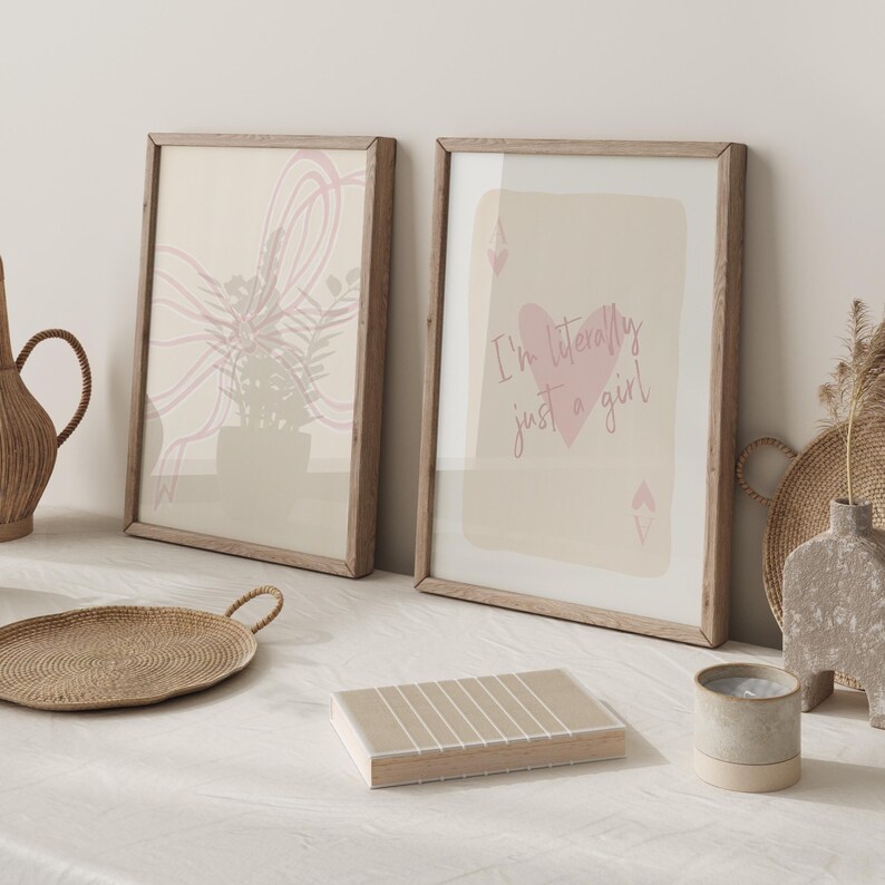May include: Two framed art prints with light wood frames. One print features an abstract floral design in pink and beige. The other print has a pink heart and the text "I'm literally just a girl".