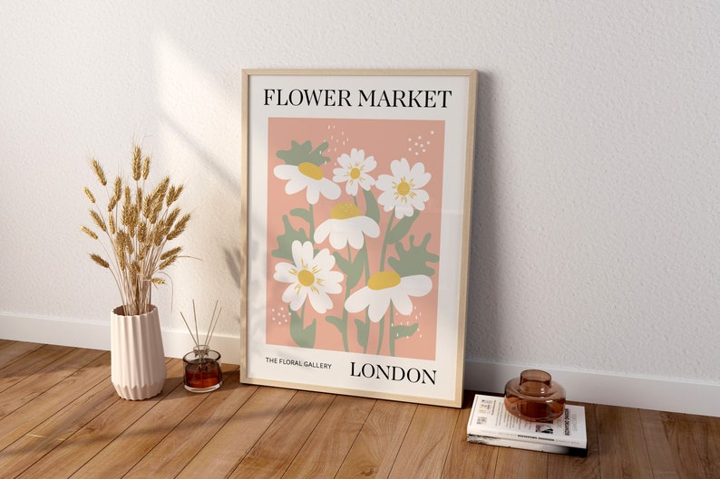 May include: A framed poster with a pink background and a floral illustration of white daisies with yellow centers. The poster reads "FLOWER MARKET" at the top, "THE FLORAL GALLERY" at the bottom left, and "LONDON" at the bottom right.