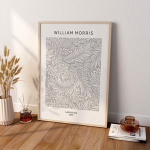 May include: A framed print featuring a floral pattern in gray and white, with the text "WILLIAM MORRIS" at the top and "LARKSPUR 1875" at the bottom. The print is displayed on a wooden floor, next to a vase with wheat stalks.