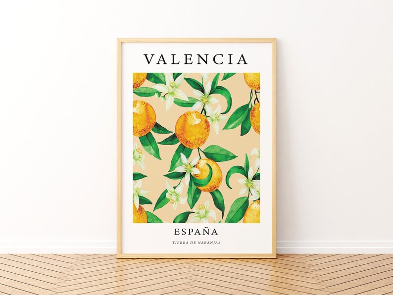 Op de afbeelding: Een ingelijst print met een aquarel-illustratie van sinaasappelbloesems en sinaasappelen op een licht beige achtergrond. De tekst "VALENCIA" staat bovenaan de print en "ESPA&Ntilde;A TIERRA DE NARANJAS" staat onderaan.