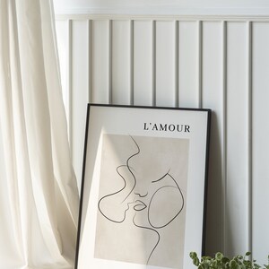 May include: A black framed print with a beige background and a line drawing of two faces. The text "L'AMOUR" is at the top of the print.