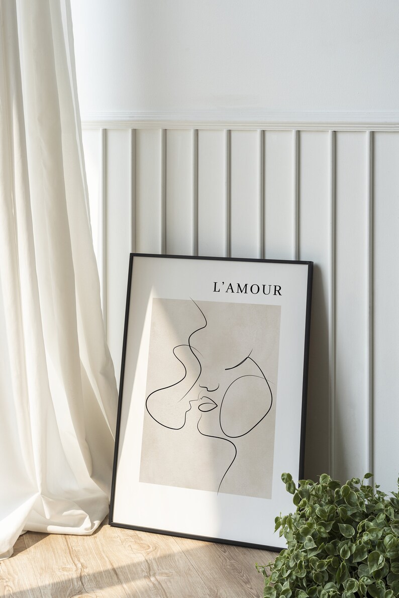 May include: A black framed print with a beige background and a line drawing of two faces. The text "L'AMOUR" is at the top of the print.