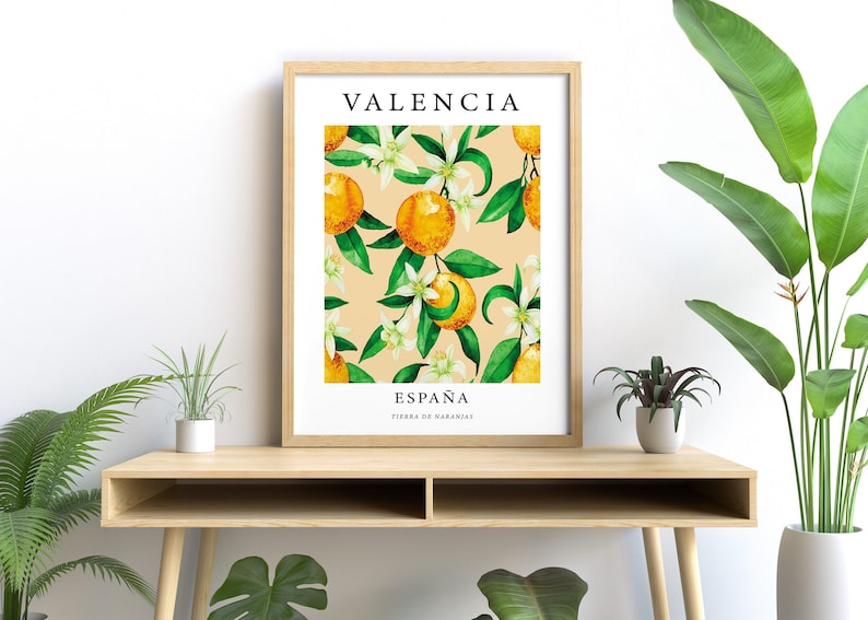 Op de afbeelding: Een ingelijst print met een aquarel-illustratie van sinaasappelbloesems en sinaasappelen op een perzikkleurige achtergrond. De tekst "VALENCIA" staat bovenaan de print en "ESPA&Ntilde;A TIERRA DE NARANJAS" staat onderaan.