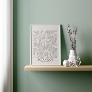 May include: A white framed print with a botanical illustration of purple and green leaves. The print is on a wooden shelf with a white vase and a white geometric object.