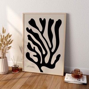 May include: A black and white abstract print of a stylized branch with a beige background. The print is framed in a light wood frame.