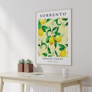 May include: A framed print with a yellow background featuring a watercolor illustration of lemon trees with green leaves and white flowers. The text "SORRENTO AMALFI COAST ALBERI DI LIMONE" is printed below the illustration.
