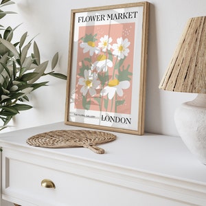 May include: A framed print with a pink background and white flowers. The print says "FLOWER MARKET" at the top and "THE FLORAL GALLERY LONDON" at the bottom.