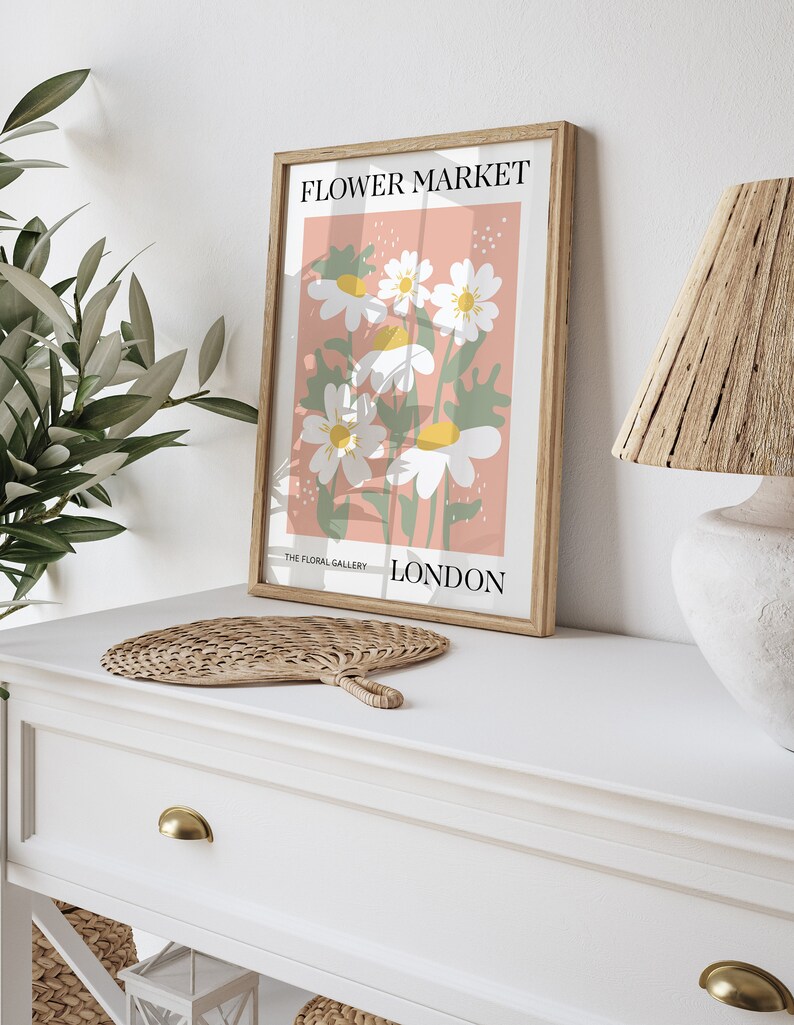 May include: A framed print with a pink background and white flowers. The print says "FLOWER MARKET" at the top and "THE FLORAL GALLERY LONDON" at the bottom.