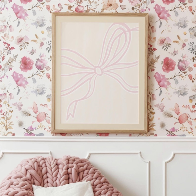 May include: A framed art print with a light pink bow design on a cream background. The artwork is in a light wood frame, set against floral wallpaper. The bow is a simple, elegant design, suitable for home decor and interior design.