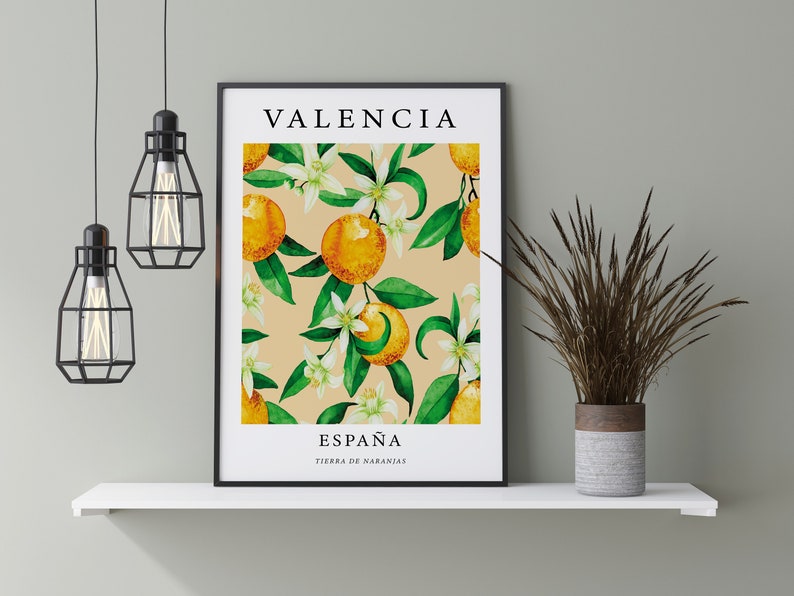 Op de afbeelding: Een ingelijst afdruk met een aquarel-illustratie van sinaasappelbloesems en sinaasappelen. De afdruk bevat de tekst "Valencia, Espa&ntilde;a, Tierra de Naranjas" in zwart.
