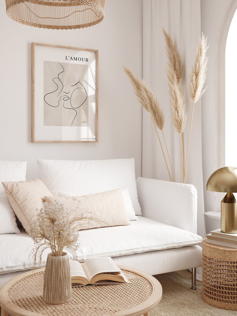 May include: A white sofa with a beige throw pillow and a vase of dried flowers on a coffee table. A framed print with the text "L'AMOUR" hangs on the wall above the sofa. Dried pampas grass is in a vase on the floor next to the sofa.
