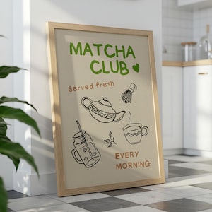 Pu&ograve; includere: Un cartello incorniciato con le parole "Matcha Club" in verde, e "Served fresh" e "Every morning" in marrone. Il cartello presenta disegni a tratto di oggetti legati al matcha, tra cui una teiera, una tazza e una frusta.