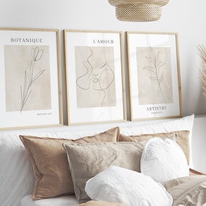 K&ouml;nnte beinhalten: Drei gerahmte minimalistische Line-Art-Drucke mit beigefarbenem Hintergrund. Die Drucke zeigen eine Blume, die Gesichter eines Paares und ein Blatt. Die Drucke sind mit "Botanique", "L'Amour" und "Artistry" betitelt.