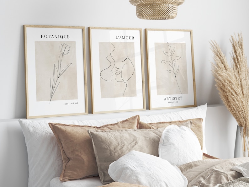 K&ouml;nnte beinhalten: Drei gerahmte minimalistische Line-Art-Drucke mit beigefarbenem Hintergrund. Die Drucke zeigen eine Blume, die Gesichter eines Paares und ein Blatt. Die Drucke sind mit "Botanique", "L'Amour" und "Artistry" betitelt.