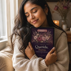 May include: A dark purple book titled Querida, Sana. Tu Diario de Sanación Emocional, featuring a detailed floral illustration of pink and white roses on the cover, with the text Edición Especial Para Mujeres Lejanas and the brand name Livvora.