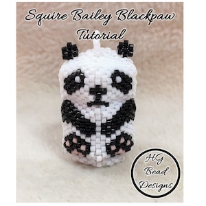 May include: A beaded panda charm with black and white beads, and pink accents on the paws. The charm is labelled "Squire Bailey Blackpaw Tutorial" and "HG Bead Designs".