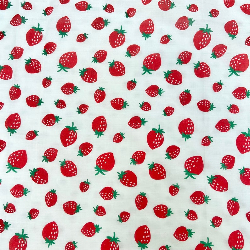 May include: White fabric with a repeating pattern of red strawberries. The strawberries are scattered randomly across the fabric.