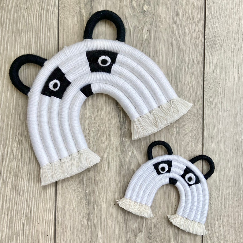 Puede incluir: Dos arco&iacute;ris de macram&eacute; de panda blanco y negro con flecos. El arco&iacute;ris m&aacute;s grande est&aacute; a la izquierda y el m&aacute;s peque&ntilde;o a la derecha.