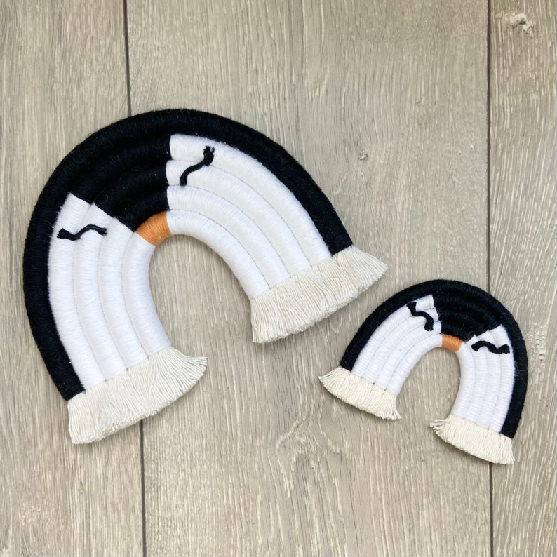 Op de afbeelding: Twee zwart-witte macram&eacute; regenbogen met franjes. De grotere regenboog heeft een kleine oranje streep.