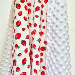 May include: A white and red fabric with a strawberry pattern on one side and a white textured fabric on the other side. The fabric is folded in half and the two sides are visible.