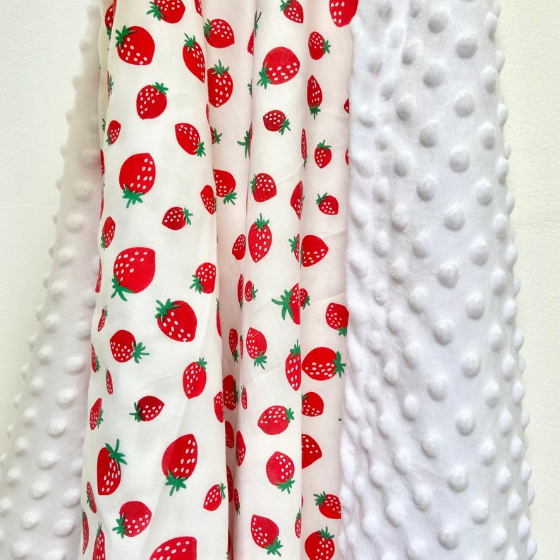 May include: A white and red fabric with a strawberry pattern on one side and a white textured fabric on the other side. The fabric is folded in half and the two sides are visible.