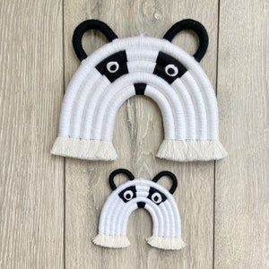 Puede incluir: Dos tapices de pared de arco&iacute;ris de crochet blanco y negro con un dise&ntilde;o de cara de mapache. El arco&iacute;ris m&aacute;s grande mide aproximadamente 30 cm de ancho y el arco&iacute;ris m&aacute;s peque&ntilde;o mide aproximadamente 15 cm de ancho.