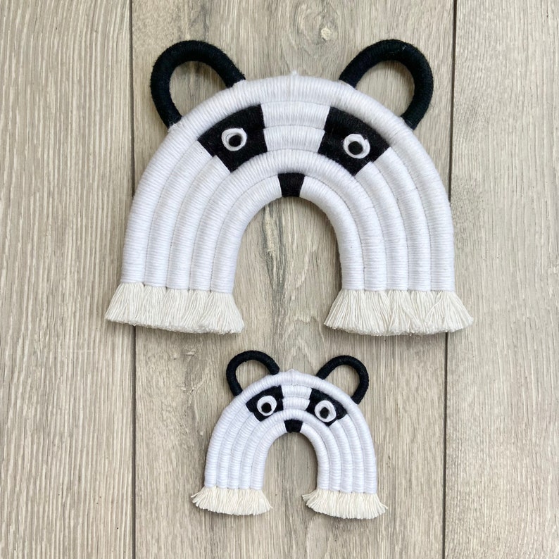 Puede incluir: Dos tapices de pared de arco&iacute;ris de crochet blanco y negro con un dise&ntilde;o de cara de mapache. El arco&iacute;ris m&aacute;s grande mide aproximadamente 30 cm de ancho y el arco&iacute;ris m&aacute;s peque&ntilde;o mide aproximadamente 15 cm de ancho.