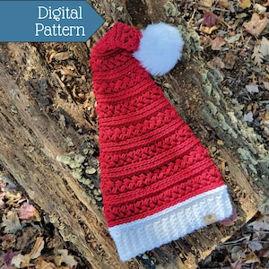 May include: A red and white crocheted Santa hat with a white pom-pom on top. The hat is lying on a log with autumn leaves around it.